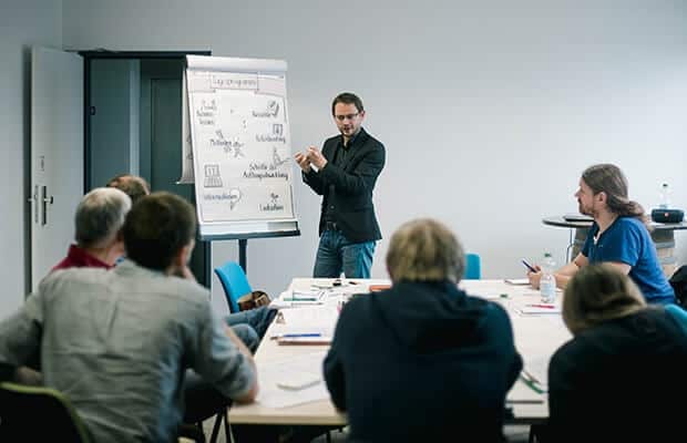 Seminarraum der ISH Akademie: Teilnehmende arbeiten an Tischen, ein Dozent moderiert am Flipchart